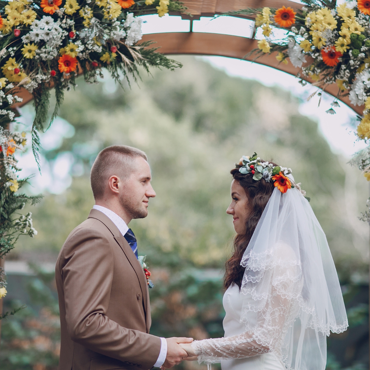 bride and groom under arch covered with Summer flowers